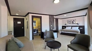 Quarto de hotel com cama, sofá, poltrona, mesinha e banheiro visível através de uma porta aberta.