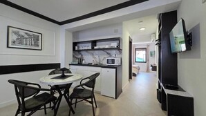 A compact kitchen with a dining area, featuring a microwave, shelves with dishes, and a TV mounted on the wall.