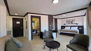 A hotel room with a bed, a sofa, a chair, a small table, and a bathroom visible through an open door.