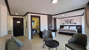 Quarto de hotel com cama, sofá, poltrona, mesinha e banheiro visível através de uma porta aberta.