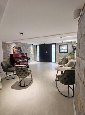 Ampla sala de estar com piano, assentos confortáveis, parede de destaque em pedra e uma grande janela.