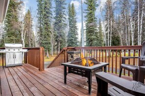 A deck with a grill and a fire pit, surrounded by a forest. - Aurora Lights on Rural 3 Acre Setting (North Pole)