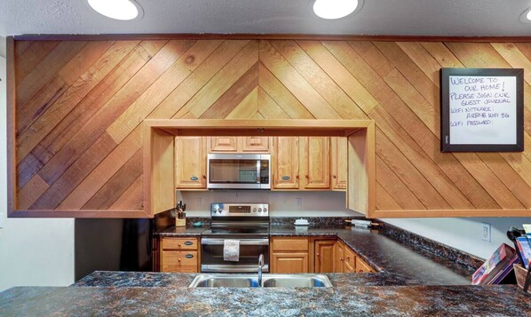 A kitchen with wooden cabinetry, a microwave, an oven, and a granite countertop. - Aurora Lights on Rural 3 Acre Setting (North Pole)