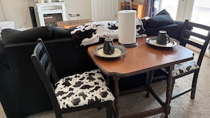 Ein Wohnzimmer mit einem schwarzen Sofa, einem Holztisch und einem Esstisch mit Stühlen.