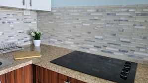 Una cocina con encimera de granito, placa de cocción por inducción negra, armarios de madera y salpicadero azulejado.