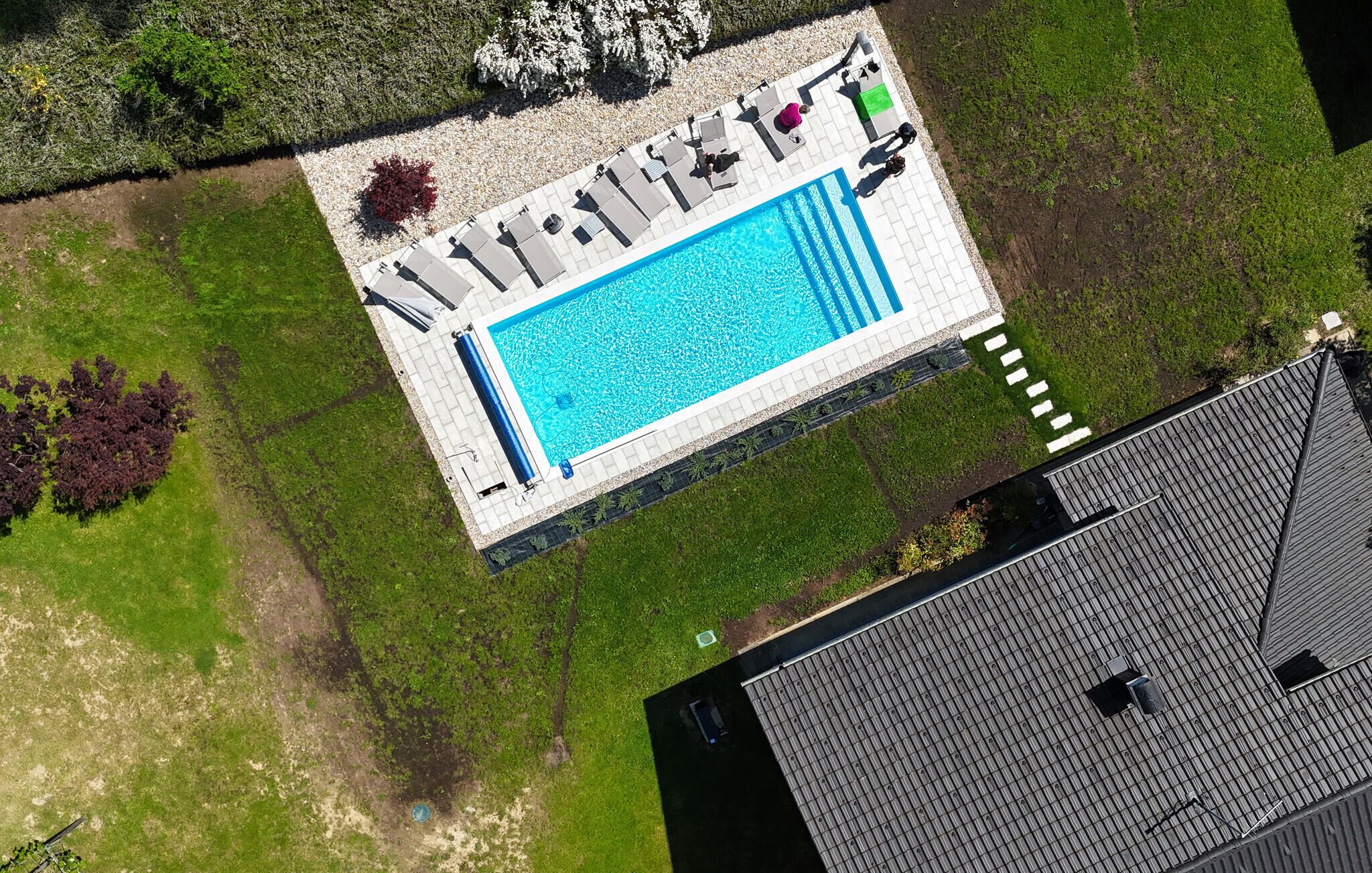 Luftaufnahme eines Schwimmbeckens mit Liegestühlen und einer gefliesten Terrasse.