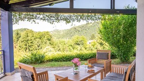 An outdoor dining area with a table and chairs, a vase with flowers, and a view of a lush green landscape.