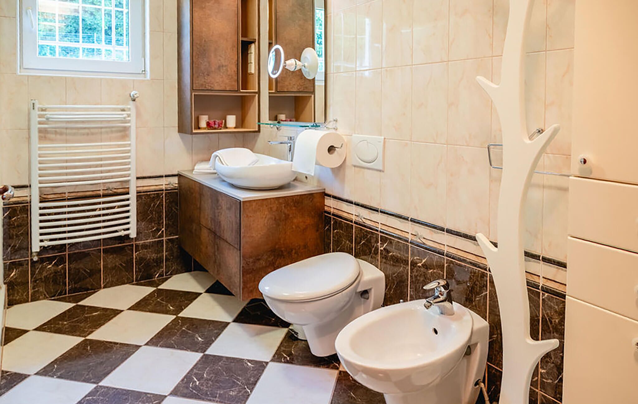 Une salle de bain avec un carrelage à motifs géométriques, des toilettes, un bidet, un lavabo, un porte-serviettes et un miroir.