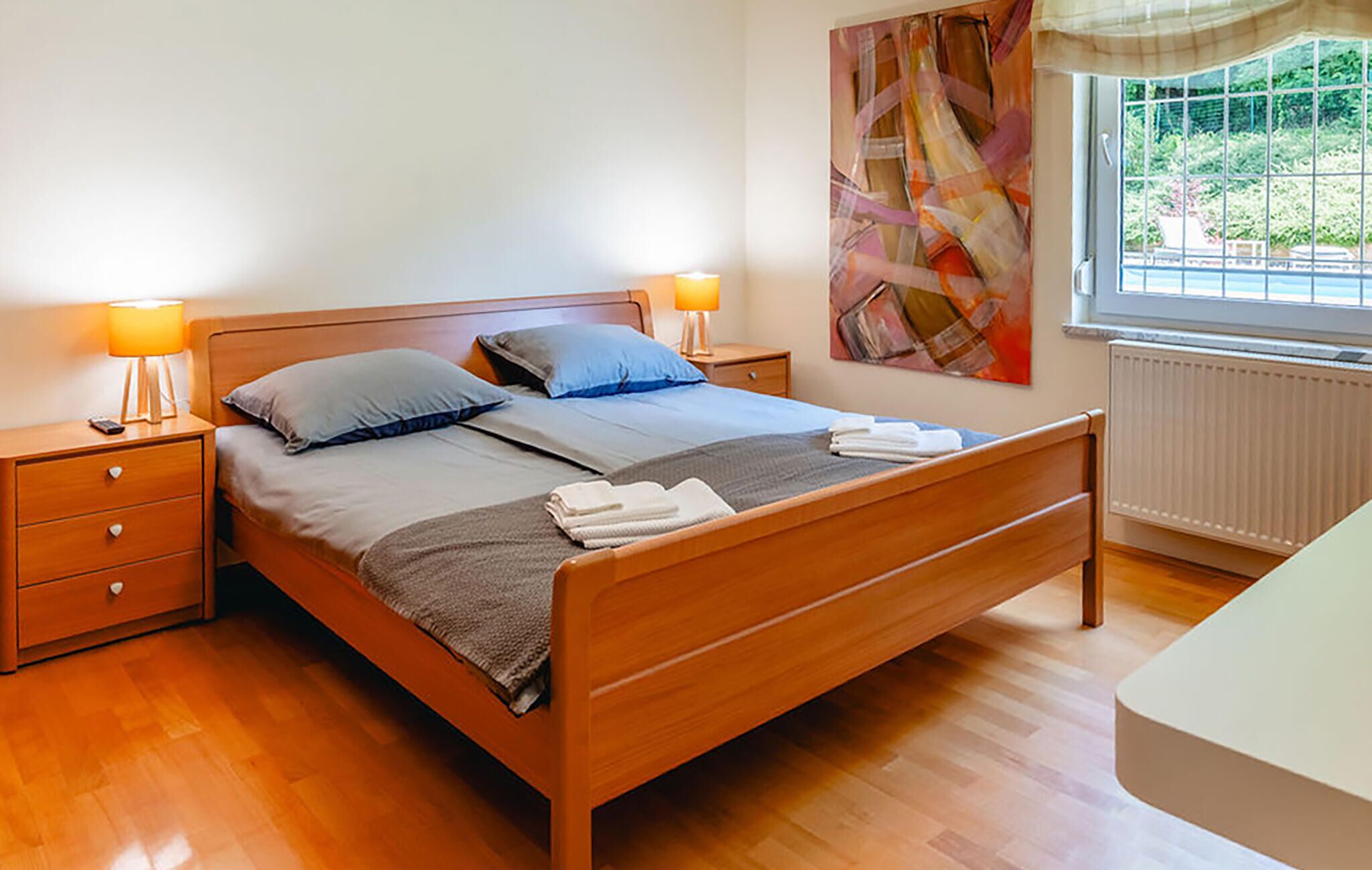 A neatly made bed with a grey and blue duvet, wooden headboard, and two bedside tables with lamps.