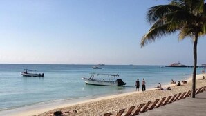 Una spiaggia con lettini e un pontile di legno, barche sull'acqua e un cielo sereno.