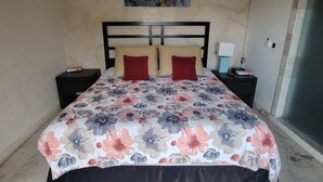 Un letto con copriletto floreale, due comodini con lampade, un condizionatore d'aria a muro e un quadro con fiori sopra il letto.