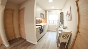 A compact kitchen with wooden cabinets, a built-in oven, and a dining area with a white table and chairs. - Perfecta UbicaciÓn Para Conocer Asturias (Oviedo)