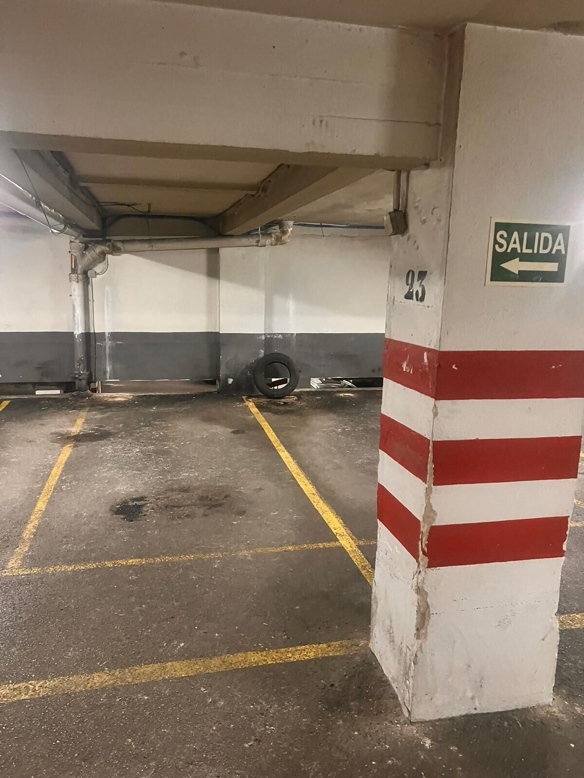 A parking garage with marked parking spaces, a 'SALIDA' sign, and a tire against the wall.