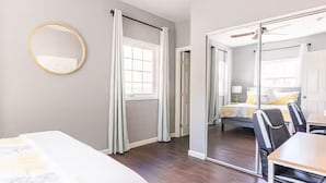 A hotel room with a bed, a desk, a chair, a mirror, and a sliding door leading to a bathroom.