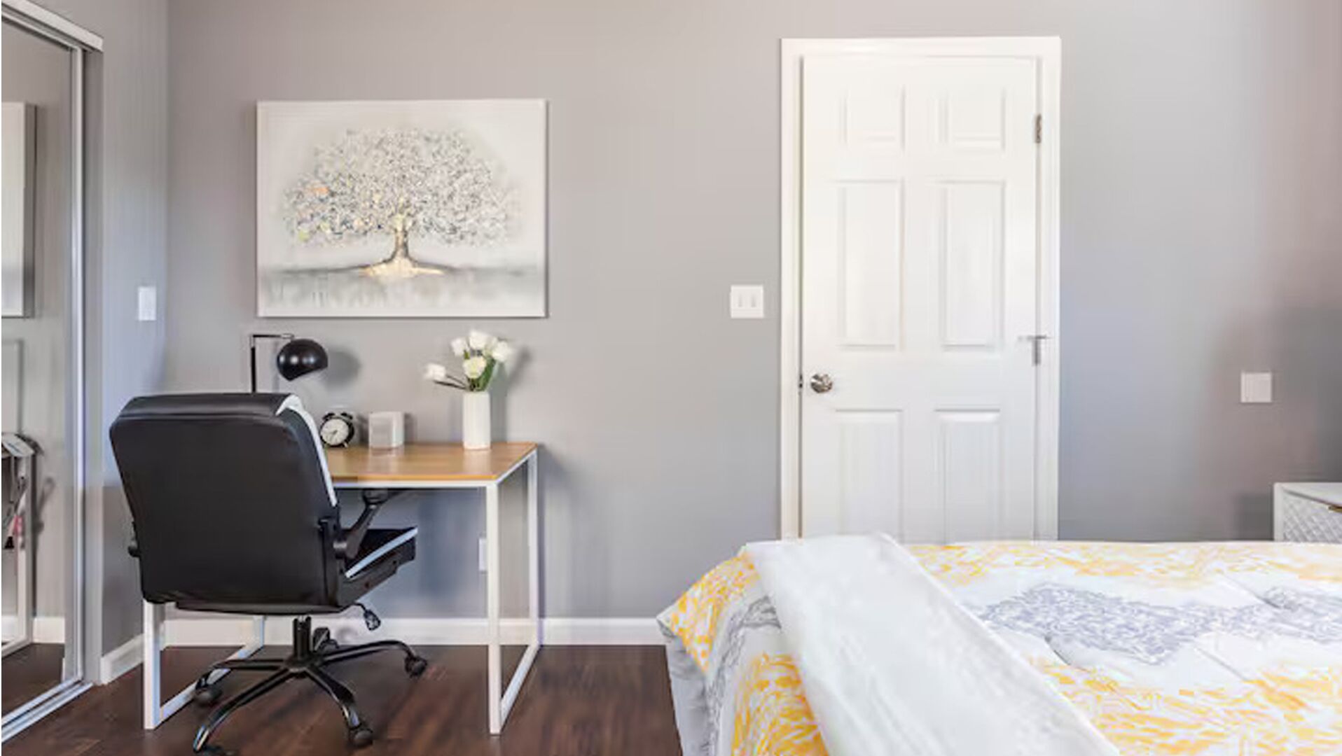 Un dormitorio con una cama, un escritorio con una silla, una puerta blanca y un cuadro colgado en la pared de un árbol.
