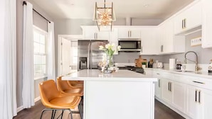A modern kitchen with white cabinetry, a central island with seating, and a decorative light fixture.