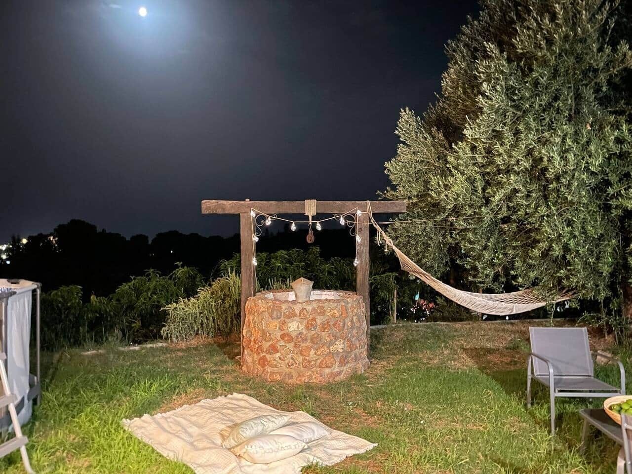 A stone fire pit with a wooden pergola overhead, surrounded by grass and a hammock.