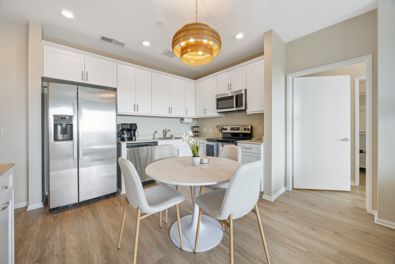 A modern kitchen with white cabinets, stainless steel appliances, and a round dining table with chairs.
