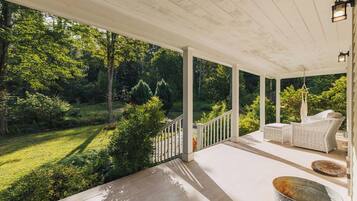 Une véranda couverte avec des balustrades blanches, des meubles en osier et un seau en métal.