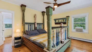 Una camera da letto con un letto a baldacchino, una ventola a soffitto, una finestra con condizionatore d'aria e una porta che dà su un'altra stanza.