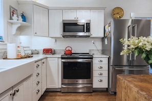 Una cocina moderna con armarios blancos, electrodomésticos de acero inoxidable, un microondas, horno y refrigerador.