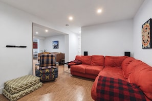Una sala moderna con un sofá rojo, un sillón estampado y un pequeño banquito verde.