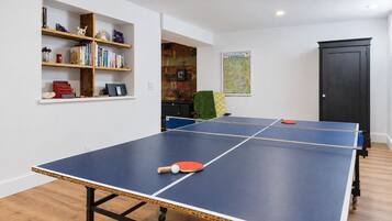Une table de ping-pong avec deux raquettes, une bibliothèque remplie de livres et d’objets décoratifs, et une carte accrochée au mur.