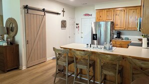 A kitchen with wooden cabinets, a stainless steel refrigerator, a sink, and a dining area with four chairs.