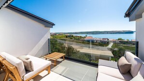 A balcony with two sofas and a small table, overlooking a coastal area with houses and a body of water. - Amazing home in Razanac (Razanac)