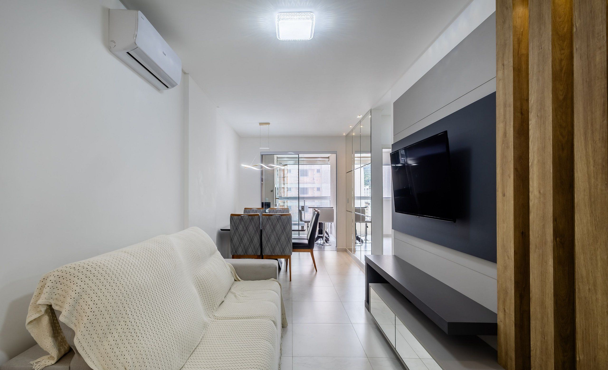 A modern living room with a sofa, a flat-screen TV, and a dining area in the background.