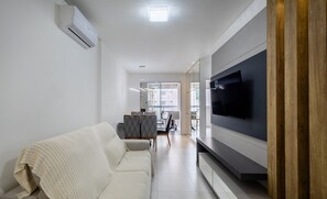 A modern living room with a sofa, a flat-screen TV, and a dining area in the background. - 2BR apt w/ Bbq, 800m From Beach Cba0902 (Itapema)