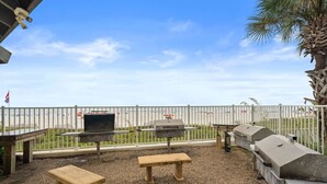 An outdoor patio with a grill, benches, and a view of the beach.