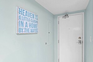 A room with a light blue wall, a white door, and a sign with blue text. - Beachfront Condo at Windward Pointe! (Orange Beach)
