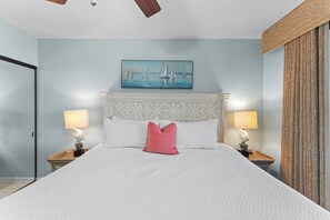 A bed with a white headboard, two bedside lamps, a painting of sailboats, and a wooden headboard on the right. - Beachfront Condo at Windward Pointe! (Orange Beach)