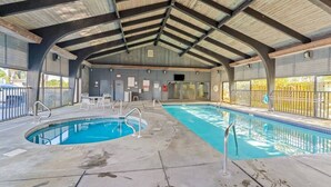 An indoor swimming pool with a covered roof, clear poolside area, and a view of the outside.