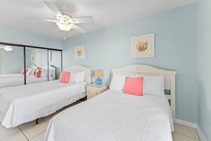 A hotel room with two beds, a ceiling fan, a nightstand with a lamp, and framed artwork on the walls.