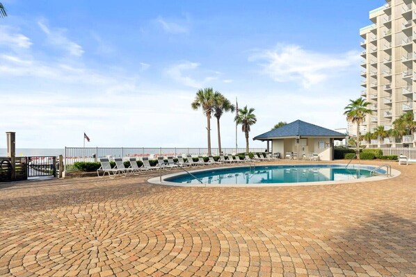 A pool area with lounge chairs, a small building, and a tall hotel structure. - Beachfront Condo at Windward Pointe! (Orange Beach)