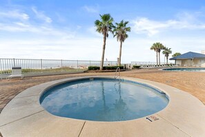 Uma piscina com um deck ao redor, palmeiras e vista para a praia.