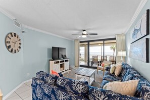 Uma sala de estar com televisão, sofá, mesa de centro e uma varanda com mobiliário externo.