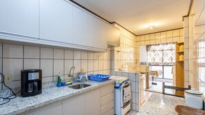 A modern kitchen with white cabinets, a coffee maker, a sink, and a window with floral curtains. - Apt w/ Balcony - Seafront in Meia Praia Ceo0104 (Itapema)