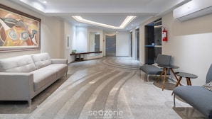 A modern lobby with a sofa, armchairs, and a coffee table. There is a painting on the wall and an air conditioning unit.