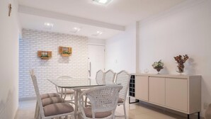 A dining area with a glass table and wicker chairs, a white brick wall, and a white cabinet with decorative items.