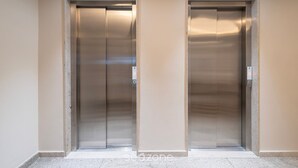 Two elevator doors in a hallway with a plain wall and a tiled floor.