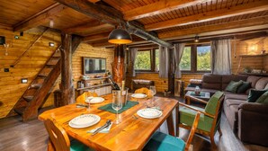 A wooden cabin interior with a dining area, a sofa, and a TV.