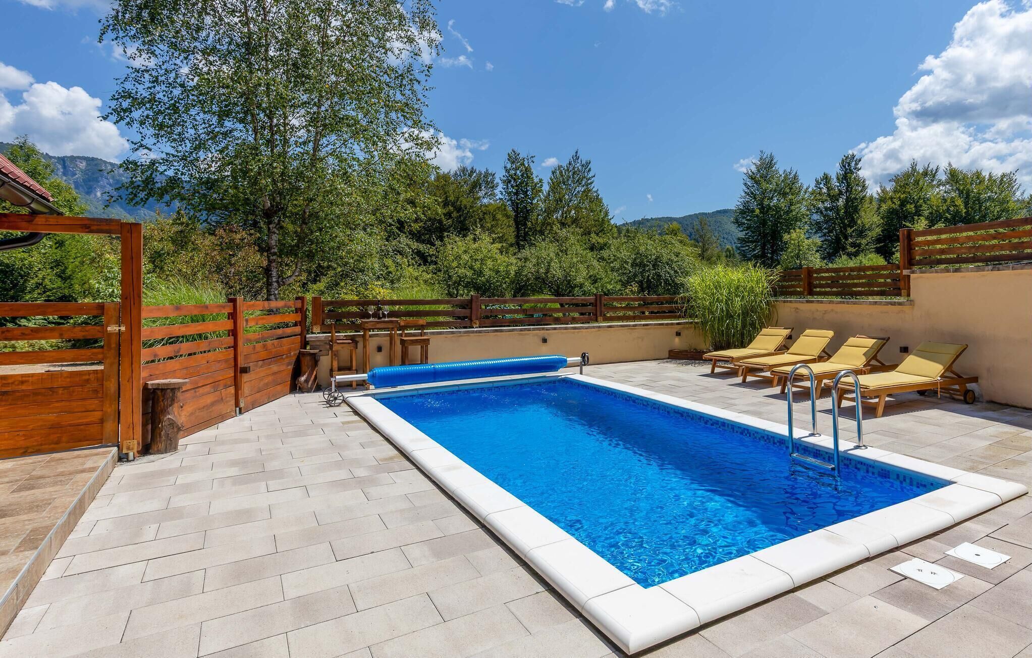 Piscina rectangular con terraza de madera, rodeada de sillas de descanso y una valla de madera.