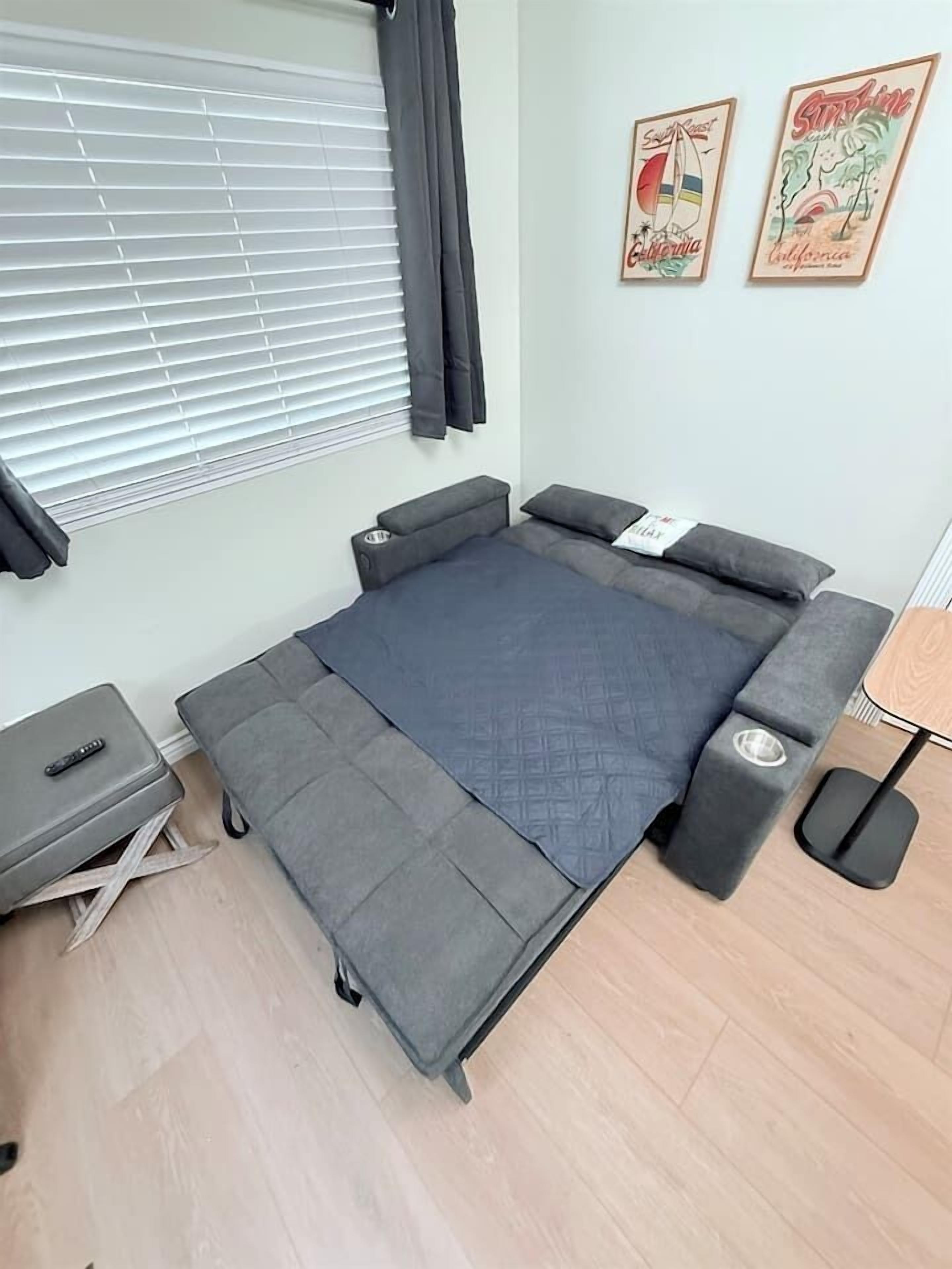 A compact bed with storage drawers, a bedside table, and a small desk with a chair.