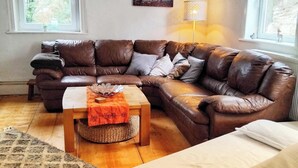 Un salon chaleureux avec un canapé d’angle en cuir marron, une petite table basse en bois et une lampe.