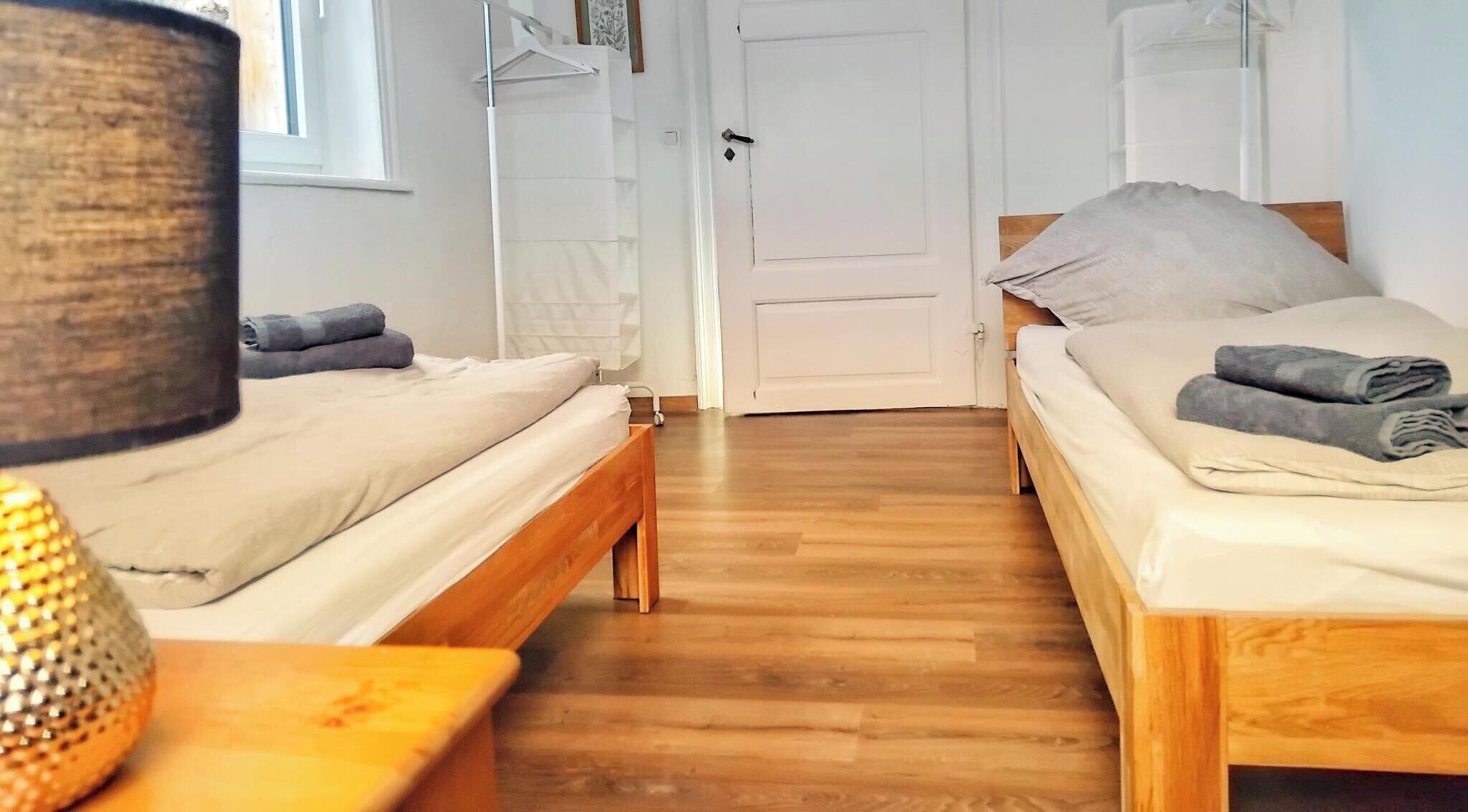 A room with two wooden beds, a lamp, and a door leading to another room.