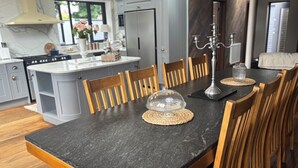 A modern kitchen with grey cabinets, a central island, and a dining area with wooden chairs and a black granite table.