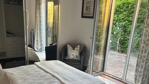 A bedroom with a bed, a chair, a wardrobe, and a sliding glass door leading to a balcony.